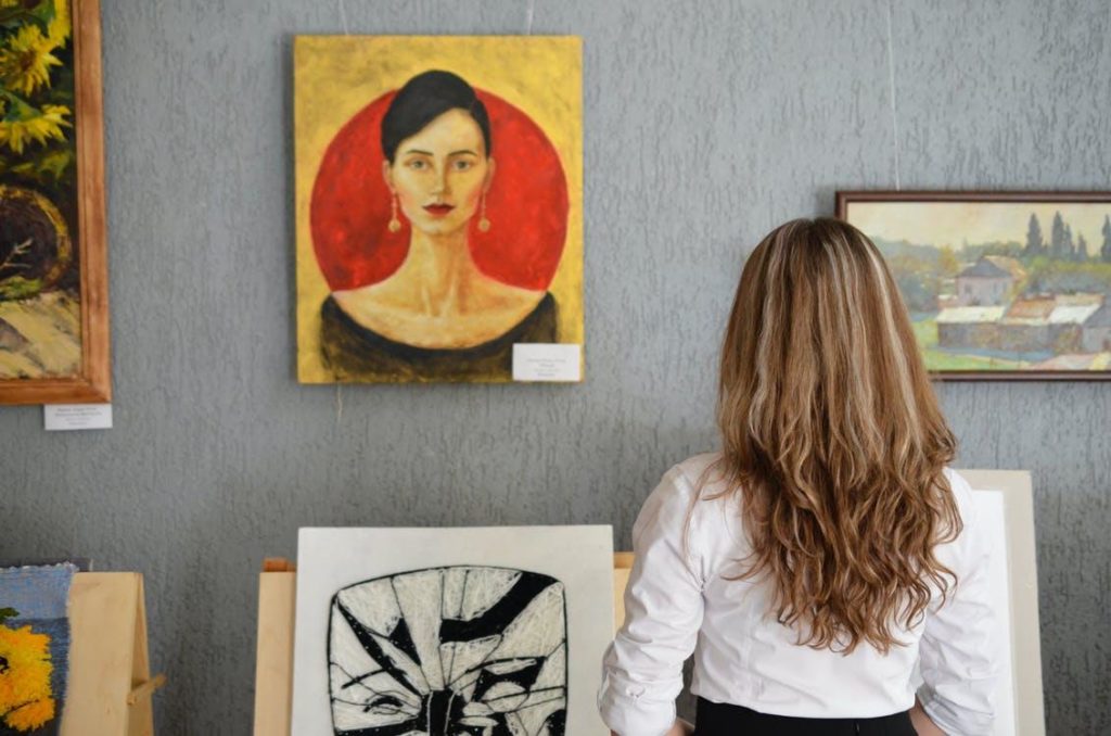 Woman Looking At Paintings Displayed On The Wall
